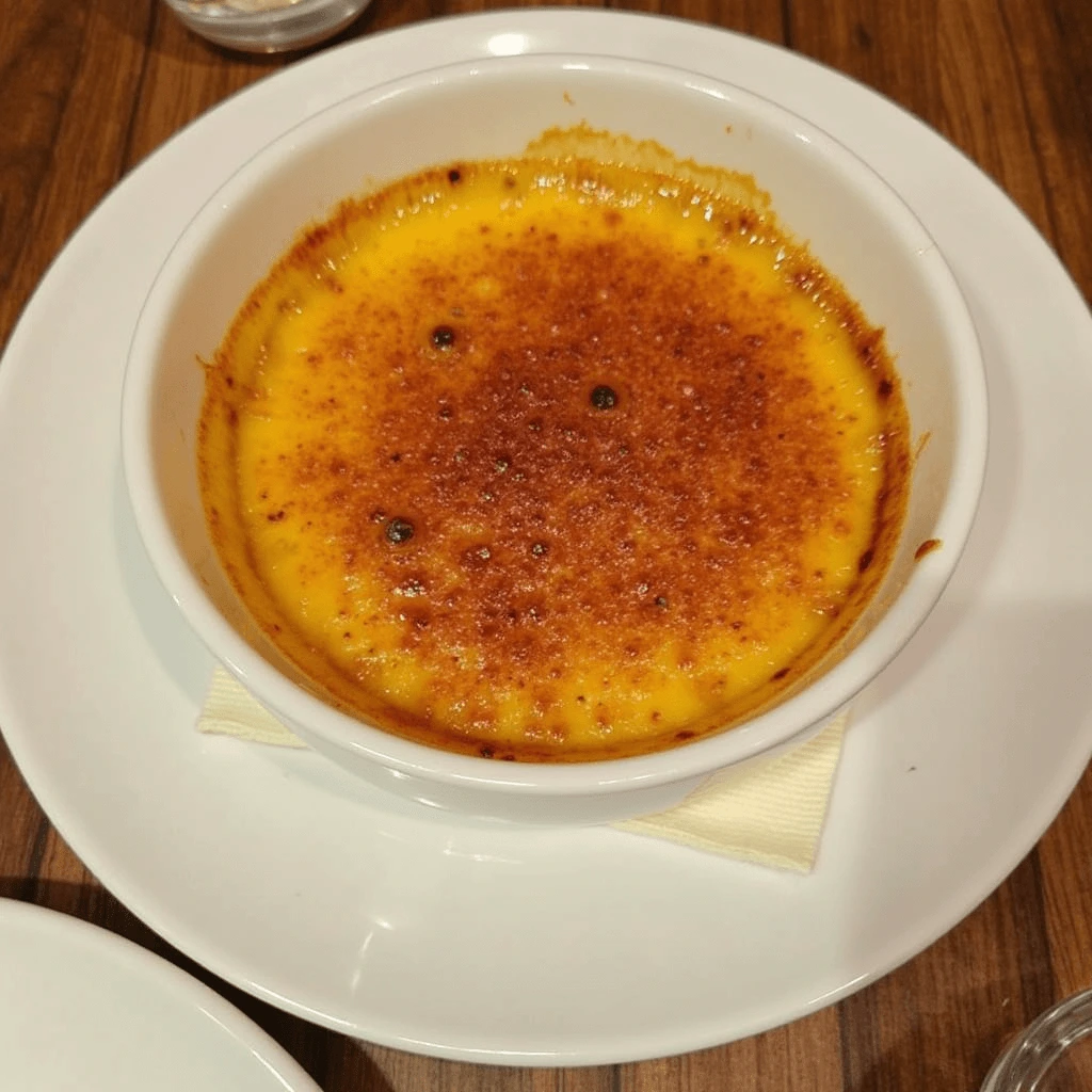 "Golden caramelized Crab Brûlée served in a ramekin with a crispy crust, garnished with fresh herbs on a rustic wooden table."